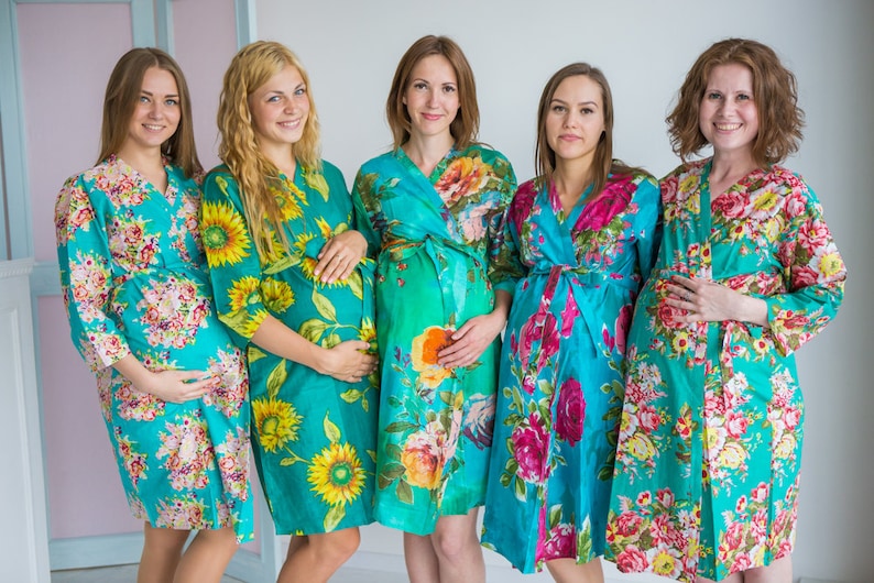 K&ouml;nnte beinhalten: F&uuml;nf Frauen in passenden Roben mit t&uuml;rkisfarbenem Blumendruck. Die Roben haben lange &Auml;rmel und werden in der Taille gebunden. Die Frauen l&auml;cheln und schauen in die Kamera.
