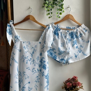 Op de afbeelding: Een witte pyjamaset met een blauwe bloemenprint. Het topje heeft een vierkante halslijn en strikbandjes. De shorts hebben een elastische tailleband en een trekkoord.