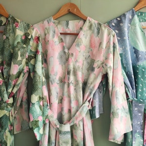 Könnte beinhalten: Drei langärmelige Roben mit Blumenmustern. Die Robe links hat ein grünes und rosafarbenes Blumenmuster, die mittlere Robe hat ein rosafarbenes und weißes Blumenmuster und die Robe rechts hat ein blaues und grünes Blumenmuster.