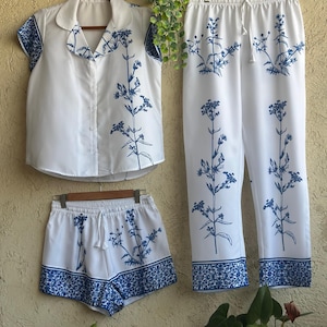 Op de afbeelding: Witte pyjamaset met een blauwe bloemenprint. De set bevat een shirt met korte mouwen, een short en een broek.
