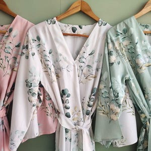 May include: Three floral print robes in pink, white, and light green. The robes have long sleeves and a V-neckline. They are tied at the waist with a matching sash.