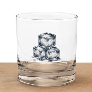 Może przedstawiać: Przezroczysty szklany tumbler z wzorem trzech kostek lodu z przodu. Tumbler stoi na drewnianej powierzchni.