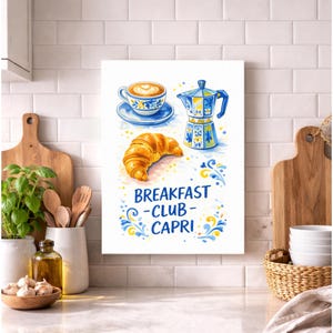 May include: A watercolor-style print featuring a coffee cup, espresso maker, and croissant. The print has a blue and yellow color scheme with the words "BREAKFAST - CLUB - CAPRI" in the center. The image is on a white background.