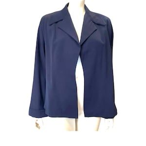 May include: A solid navy blue open-front jacket featuring a notched collar, long sleeves with folded cuffs, and a straight hemline. The garment is displayed on a mannequin, showcasing a simple, structured design with no visible buttons or closures.
