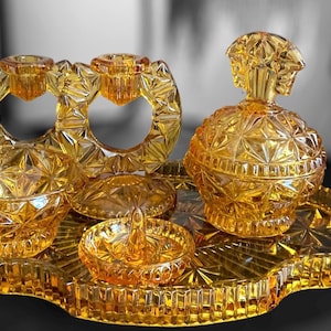 Könnte beinhalten: Ein Vintage-Schminktisch-Set aus bernsteinfarbenem Glas mit einem Tablett, einem Ringhalter, einer kleinen Schale, einer größeren Schale und einer Flasche mit Deckel. Das Set hat ein geometrisches Muster.