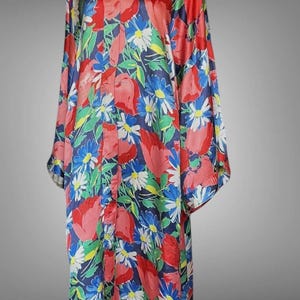 May include: A long-sleeved robe featuring a vibrant floral pattern with red, blue, white, and green flowers set against a dark blue background. The garment has a V-neckline, a button-down front closure, and a loose, flowing silhouette.