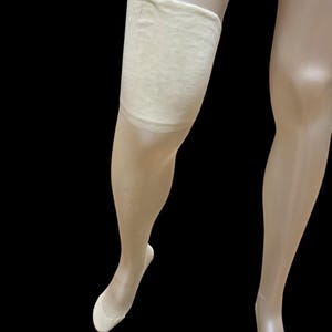 May include: A pair of nude-coloured stockings with a beige suspender belt. The suspender belt is made of a soft, stretchy material and has a smooth finish.