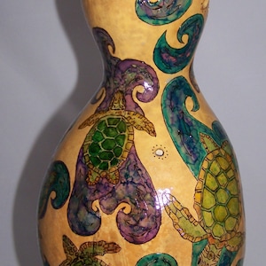 Peut inclure: Une gourde avec un fond brun clair décorée de tortues de mer peintes en vert, bleu et violet et de motifs tourbillonnants.