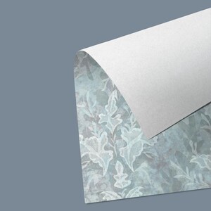 May include: A section of patterned paper with a botanical design in shades of blue and grey, with a white sheet of paper partially covering it. The botanical design features stylized leaves and floral elements.