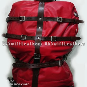 Puede incluir: Chaqueta de restricción de cuero rojo con múltiples correas de cuero marrón y hebillas plateadas. La chaqueta tiene una correa vertical de cuero marrón en el centro y el texto "UkSwiftLeathers" es visible.