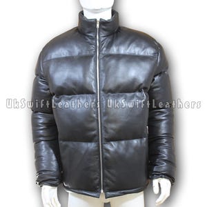 May include: Black leather puffer jacket with a high collar and a full-length silver zip. The jacket has a quilted design and is displayed on a mannequin. The text "UkSwiftLeathers" is printed on the jacket.