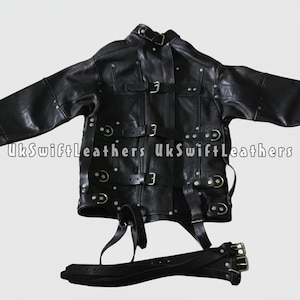 Op de afbeelding: Zwarte leren jas met meerdere riemen en gespen. De jas heeft een hoge kraag en is versierd met zilverkleurige klinknagels. De tekst "UkSwiftLeathers" is zichtbaar op de jas. Een bijpassende riem is ook inbegrepen.