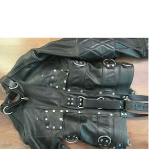 May include: Black leather jacket with multiple straps, buckles, and rings. The jacket has a quilted design on the shoulders and a zip closure.