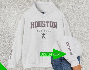Può includere: Una felpa con cappuccio grigia con il testo "HOUSTON FOOTBALL" in lettere marroni. La felpa ha una stampa personalizzata sulla manica che dice "CUSTOM #7".