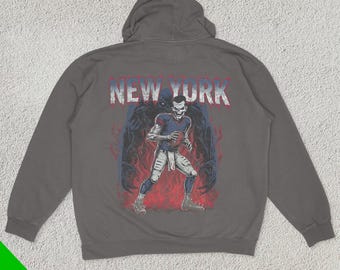 May include: A charcoal gray hooded sweatshirt with a graphic print of a football player in a blue and red uniform. The player is surrounded by a dark figure with the text "NEW YORK" above the graphic.
