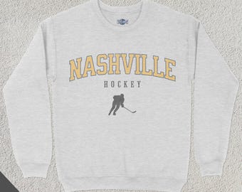 May include: A gray sweatshirt with a yellow and black Nashville Hockey logo. The logo features the word "Nashville" in a large, arched font with the word "Hockey" underneath.