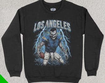 May include: Black sweatshirt featuring a graphic of a zombie football player wearing a Los Angeles Chargers jersey and holding a football. The text "Los Angeles" is printed above the graphic.