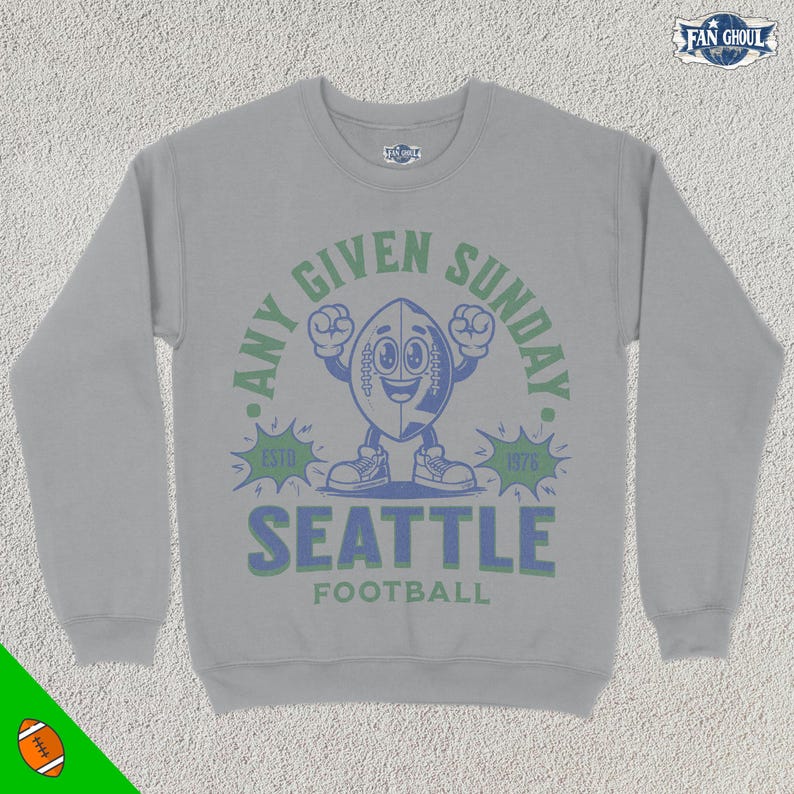May include: Gray sweatshirt with a cartoon football character wearing a blue jersey and holding a football. The text reads "Any Given Sunday" with the years "1976" and "Est. 1976" on either side of the character. The text "Seattle Football" is below the character.