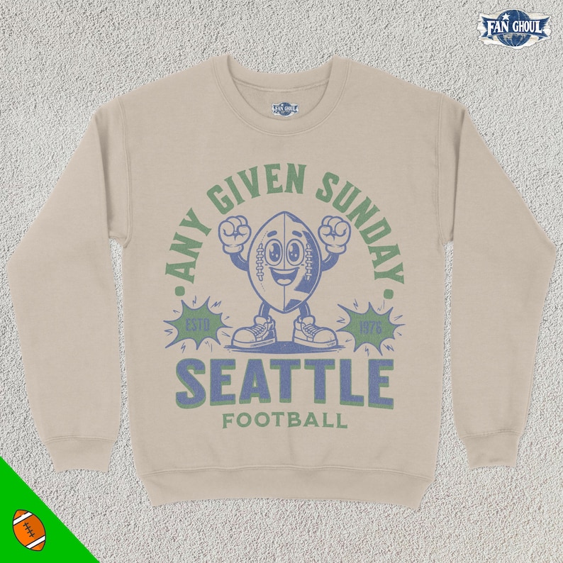 May include: Tan sweatshirt with a blue and green graphic of a cartoon football character with the text "Any Given Sunday. Est. 1976. Seattle Football."