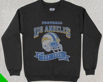 May include: Black sweatshirt featuring a vintage-style design. The design includes the words "FOOTBALL LOS ANGELES" above a football helmet with a lightning bolt, and the text "EST. 1959" on a banner below.