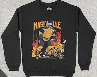 May include: Black sweatshirt with a graphic of a hockey player wearing a yellow and black jersey with the word "NASHVILLE" above him. The player is holding a hockey stick and is standing on a tiger.