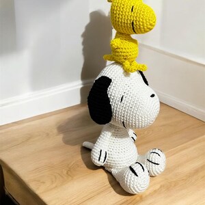 Pode incluir: Um conjunto de pel&uacute;cias Snoopy e Woodstock de croch&ecirc; artesanal. Snoopy &eacute; branco com orelhas e detalhes pretos, enquanto Woodstock &eacute; amarelo. Os brinquedos est&atilde;o em uma superf&iacute;cie de madeira. Uma adi&ccedil;&atilde;o charmosa a qualquer cole&ccedil;&atilde;o.