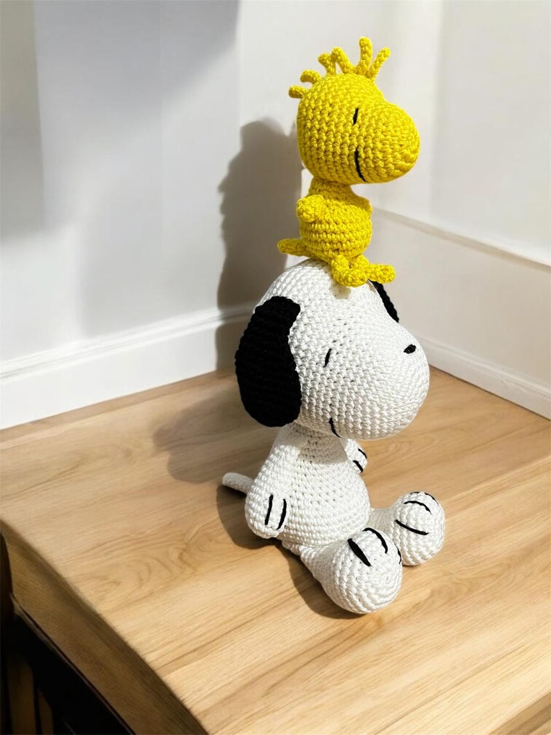 Pode incluir: Um conjunto de pel&uacute;cias Snoopy e Woodstock de croch&ecirc; artesanal. Snoopy &eacute; branco com orelhas e detalhes pretos, enquanto Woodstock &eacute; amarelo. Os brinquedos est&atilde;o em uma superf&iacute;cie de madeira. Uma adi&ccedil;&atilde;o charmosa a qualquer cole&ccedil;&atilde;o.