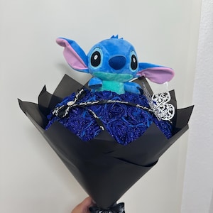 May include: A bouquet featuring a blue plush Stitch toy atop a bed of blue roses, wrapped in black paper. The bouquet is tied with a black ribbon that says "Just for you". A silver heart-shaped ornament is attached.