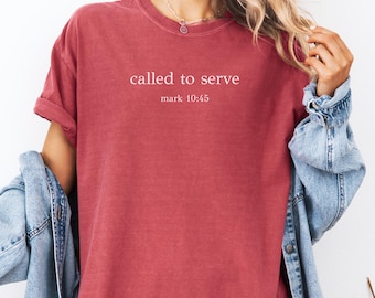 May include: Crimson-colored t-shirt with the text "called to serve" and "mark 10:45" in white. The shirt has short sleeves and a relaxed fit. A denim jacket is draped over the shoulders.