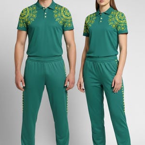 May include: Matching green athletic wear set. Includes a polo shirt with yellow floral design on the shoulders, matching pants, and a baseball cap. The set is worn with white sneakers. The polo shirt has a three-button placket.