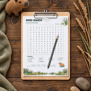 May include: A word search puzzle sheet on a wooden clipboard with a pencil resting on the grid. The sheet features the title WORD SEARCH, a letter grid, a word bank with checkboxes, and illustrations of a capybara and marshy vegetation.