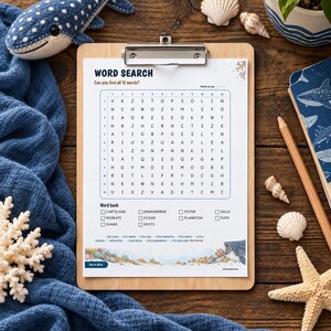 May include: A word search puzzle sheet on a wooden clipboard featuring a shark theme. The grid contains letters and a word bank with terms like Cartilage, Endangered, Filter, Gills, Migrate, Ocean, Plankton, Pups, Shark, and Spots. The bottom border displays colorful coral reef illustrations.