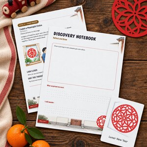 May include: Two white paper sheets titled Discovery Notebook with prompts for drawing and reflection, alongside a small card labeled Lunar New Year featuring a red circular paper-cut design, a red felt train toy, and two fresh oranges with green leaves.