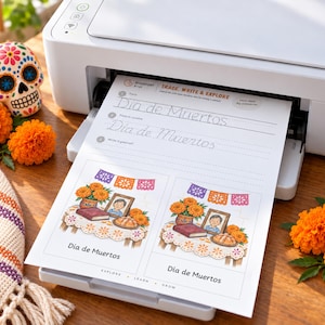 May include: A white printer outputting a worksheet titled Trace, Write & Explore Dia de Muertos. The page features handwriting practice lines and two illustrations of an altar with marigolds, a framed photo, and bread.