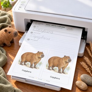 May include: A white printer outputting a worksheet titled Trace, Write & Explore with the word Capybara. The page features dotted lines for handwriting practice and two illustrations of a brown capybara. A small felt capybara toy sits nearby.