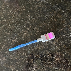 May include: A blue and white pen with a pink and white sticky note holder attached to the end.