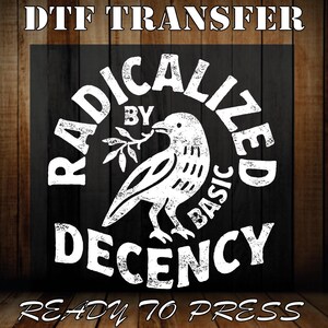 May include: A DTF transfer with a white graphic on a black background. The graphic features a bird holding a sprig, surrounded by the words "RADICALIZED BY BASIC DECENCY." The text "READY TO PRESS" is at the bottom. The background is a wood panel.