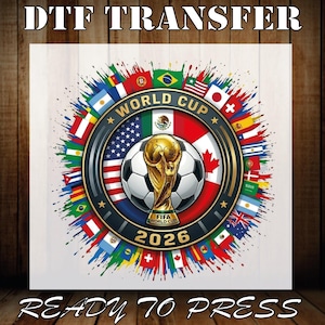 May include: A DTF transfer featuring a World Cup 2026 design. The design includes a soccer ball, the World Cup trophy, and flags from various countries. The text "READY TO PRESS" is also included.