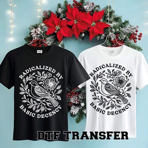 Pu&ograve; includere: Due magliette a maniche corte, una nera e una bianca, ciascuna con una grafica circolare. La grafica presenta un uccello, fiori e il testo "RADICALIZED BY BASIC DECENCY". Il testo "DTF TRANSFER" &egrave; in basso.