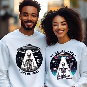 May include: Two white sweatshirts featuring a graphic of a skeleton meditating inside a UFO. The text "Take Me Away" is printed on both sweatshirts.