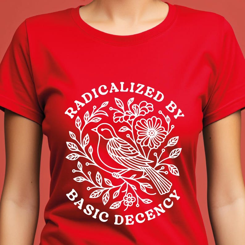 Pu&ograve; includere: T-shirt rossa con grafica bianca. La grafica raffigura un uccello su un ramo fiorito, circondato dalla scritta "RADICALIZED BY BASIC DECENCY". Il disegno &egrave; centrato sulla parte anteriore della maglietta.
