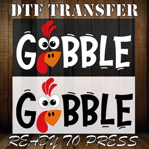 May include: DTF transfer design with the word "GOBBLE" in large white letters, incorporating a cartoon turkey face. The design is set against black and white backgrounds, with the text "READY TO PRESS" at the bottom.