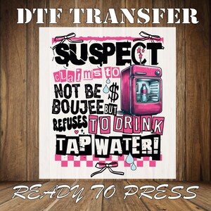 May include: Pink and black graphic design with the text "SUSPECT claims to NOT BE BOUJEE BUT REFUSES TO DRINK TAP WATER!" with a pink refrigerator illustration. The design is ready to be pressed onto a t-shirt.