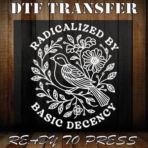 May include: White DTF transfer featuring a bird and floral design, with the text "RADICALIZED BY BASIC DECENCY". The words "DTF TRANSFER" and "READY TO PRESS" are also present. The design is on a black background.