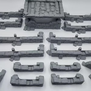 May include: A set of 14 gray 3D printed miniature sandbag walls for tabletop gaming. The walls are made of stacked blocks with a rough texture.