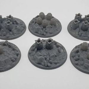 May include: Six gray plastic bases for miniature games, each featuring a different arrangement of alien pods or eggs. The bases are designed for use with tabletop games and role-playing games.