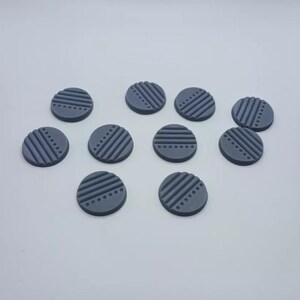 May include: Ten dark gray round gaming tokens with a geometric pattern of lines and dots.