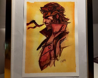 Puede incluir: Una pintura en acuarela enmarcada que muestra el perfil lateral de un personaje barbudo con cabello largo, vistiendo una chaqueta de cuello alto. La obra utiliza tonos cálidos amarillos y naranjas de fondo, con contornos en tinta marrón y roja.