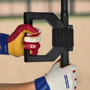 May include: Black training aid attached to a baseball bat, held by hands wearing red, yellow, and white baseball gloves. The gloves have blue wrist straps with white text. The training aid is black and has a D-shaped handle.