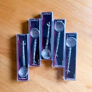 May include: Five fine pewter spoons in individual display boxes. Each spoon has a detailed handle and a round bowl with an engraved design. The boxes are dark with text that reads "FINE PEWTER" and "ETAIN FIN".